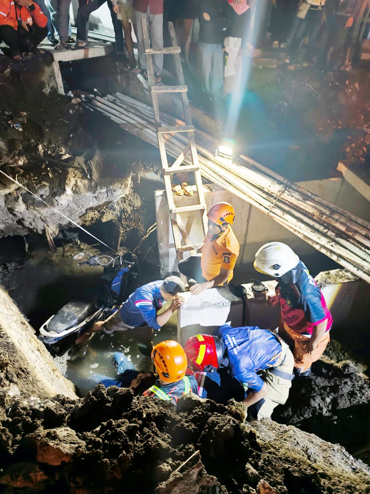Petugas gabungan melakukan evakuasi korban dan sepeda motor yang terperosok ke saluran proyek pembangunan U-Ditch di Jalan Margorejo Indah, Kecamatan Wonocolo, Surabaya, Jumat (12/6/2026) malam. Peristiwa tersebut mengakibatkan seorang perempuan lansia me